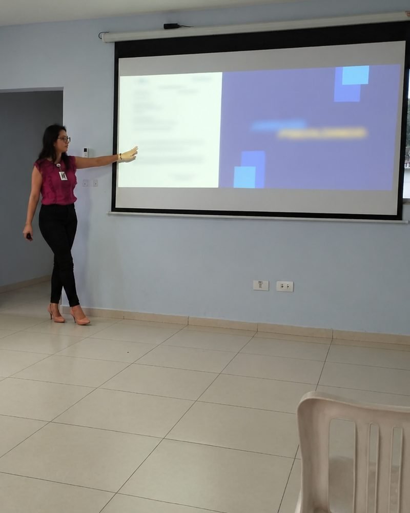 Brenda Sousa apresentando uma palestra para uma instituição, apontando para a projeção